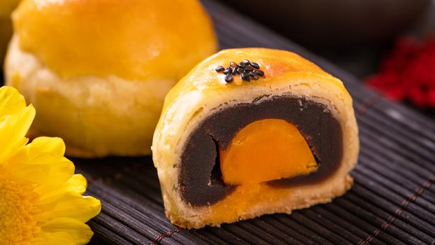 Tasty baked egg yolk pastry moon cake for Mid-Autumn Festival on black slate dark background. Chinese festive food concept, close up, copy space.