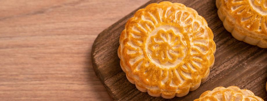Round shaped fresh baked moon cake pastry - Chinese moonckae for Mid-Autumn Moon Festival on wooden background and serving tray, top view, flat lay.