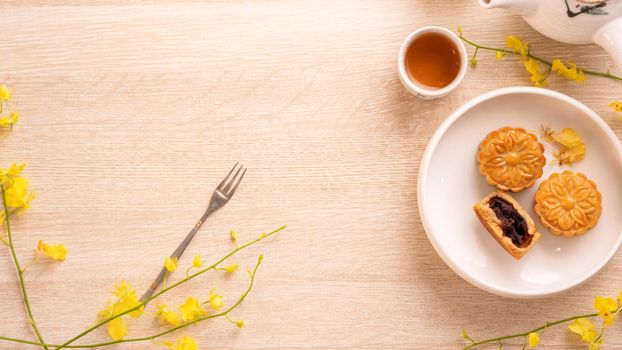 Tasty moon cake for Mid-Autumn festival on bright wooden table, concept of festive afternoon tea decorated with yellow flowers, top view, flat lay.