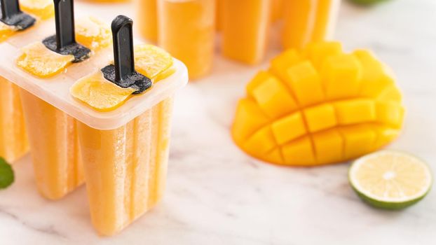 Fresh mango fruit popsicle ice in the plastic shaping box on bright marble table. Summer mood concept product design, close up.