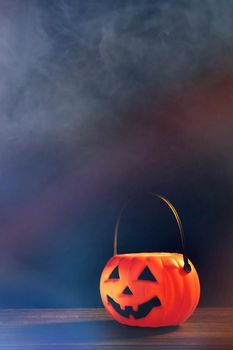 Halloween concept - Orange plastic pumpkin lantern on a dark wooden table with blurry sparkling light in the background, trick or treat, close up.