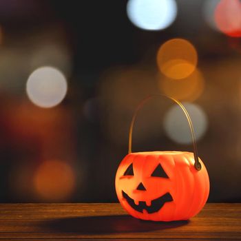 Halloween concept - Orange plastic pumpkin lantern on a dark wooden table with blurry sparkling light in the background, trick or treat, close up.