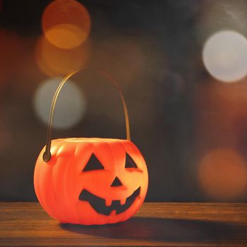 Halloween concept - Orange plastic pumpkin lantern on a dark wooden table with blurry sparkling light in the background, trick or treat, close up.