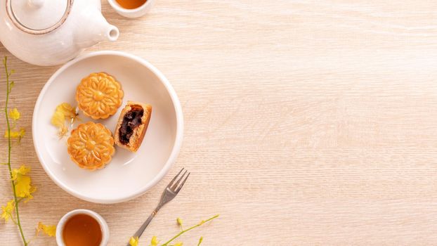 Tasty moon cake for Mid-Autumn festival on bright wooden table, concept of festive afternoon tea decorated with yellow flowers, top view, flat lay.