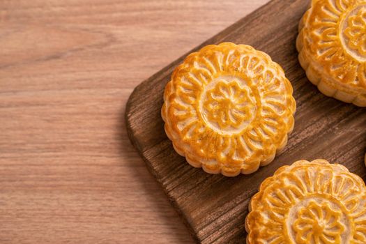 Round shaped fresh baked moon cake pastry - Chinese moonckae for Mid-Autumn Moon Festival on wooden background and serving tray, top view, flat lay.