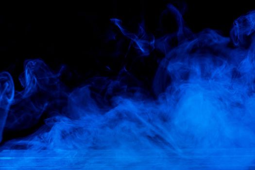 Conceptual image of blue smoke isolated on dark black background and wooden table.