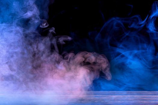 Conceptual image of multi-colored smoke isolated on dark black background and wooden table.