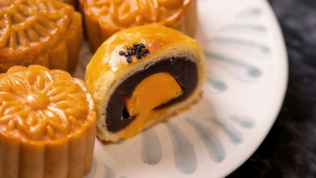 Tasty baked egg yolk pastry moon cake for Mid-Autumn Festival on black slate dark background. Chinese festive food concept, close up, copy space.