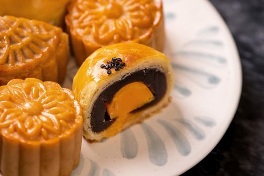 Tasty baked egg yolk pastry moon cake for Mid-Autumn Festival on black slate dark background. Chinese festive food concept, close up, copy space.