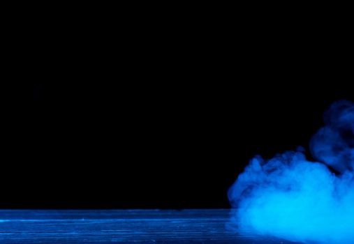 Conceptual image of blue smoke isolated on dark black background and wooden table.