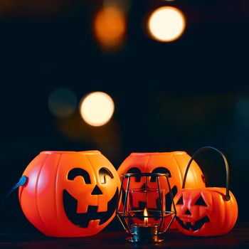 Halloween concept - Orange plastic pumpkin lantern on a dark wooden table with blurry sparkling light in the background, trick or treat, close up.
