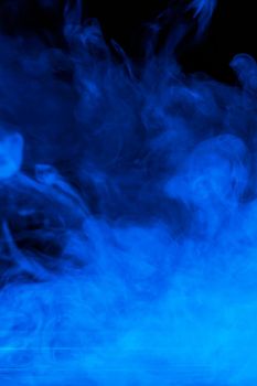 Conceptual image of blue smoke isolated on dark black background and wooden table.