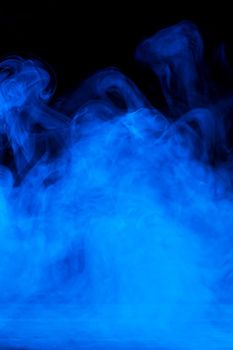 Conceptual image of blue smoke isolated on dark black background and wooden table.