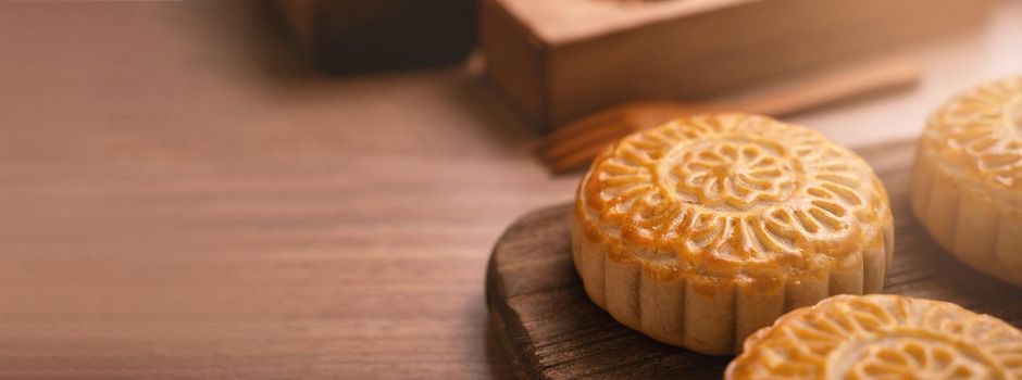 Round shaped fresh baked moon cake pastry - Chinese moonckae for Mid-Autumn Moon Festival on wooden background and serving tray, close up, copy space