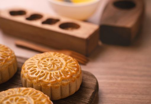 Round shaped fresh baked moon cake pastry - Chinese moonckae for Mid-Autumn Moon Festival on wooden background and serving tray, close up, copy space