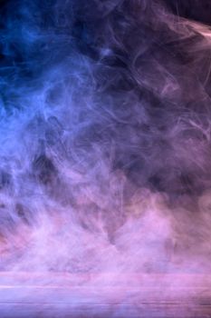 Conceptual image of multi-colored smoke isolated on dark black background and wooden table.