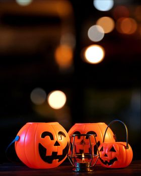 Halloween concept - Orange plastic pumpkin lantern on a dark wooden table with blurry sparkling light in the background, trick or treat, close up.