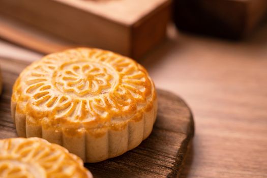 Round shaped fresh baked moon cake pastry - Chinese moonckae for Mid-Autumn Moon Festival on wooden background and serving tray, close up, copy space
