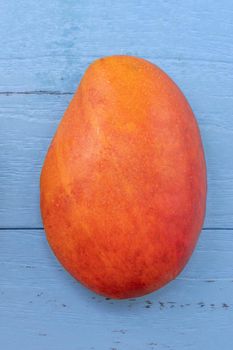 Fresh mango - beautiful chopped fruit with green leaves on bright blue timber background. Tropical fruit design concept. Flat lay. Top view. Copy space
