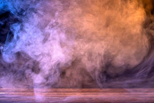 Conceptual image of multi-colored smoke isolated on dark black background and wooden table.