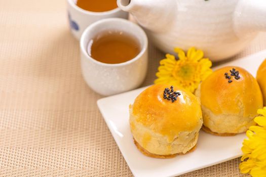 Tasty baked egg yolk pastry moon cake for Mid-Autumn Festival on bright wooden table background. Chinese festive food concept, close up, copy space.