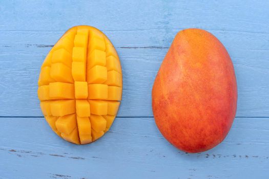 Fresh mango - beautiful chopped fruit with green leaves on bright blue timber background. Tropical fruit design concept. Flat lay. Top view. Copy space