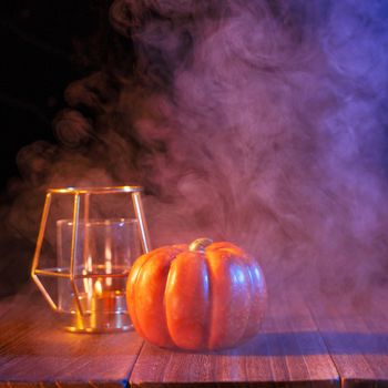 Halloween concept, orange pumpkin lantern and candles on a dark wooden table with blue-orange smoke around the background, trick or treat, close up