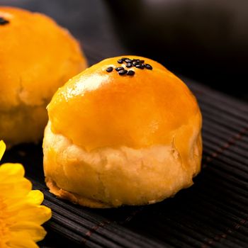 Tasty baked egg yolk pastry moon cake for Mid-Autumn Festival on black slate dark background. Chinese festive food concept, close up, copy space.