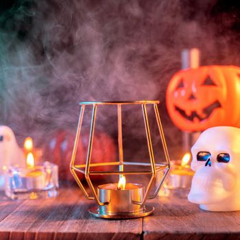 Halloween concept, orange pumpkin lantern and candles on a dark wooden table with green-orange smoke around the background, trick or treat, close up