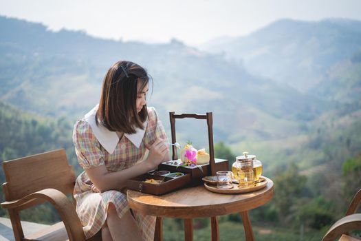 beautiful women eating cake and drinking hot green tea sitting on the chair mountain view