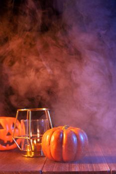 Halloween concept, orange pumpkin lantern and candles on a dark wooden table with blue-orange smoke around the background, trick or treat, close up
