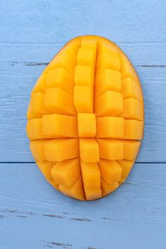 Fresh mango - beautiful chopped fruit with green leaves on bright blue timber background. Tropical fruit design concept. Flat lay. Top view. Copy space
