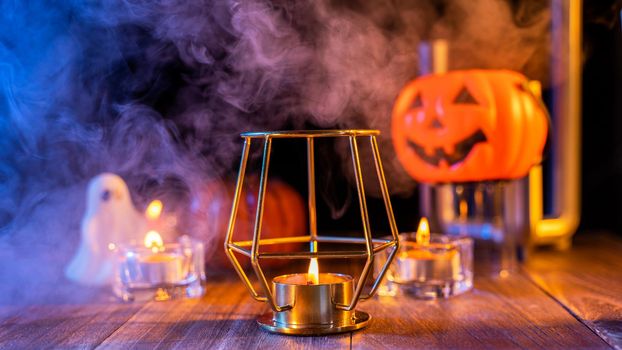 Halloween concept, orange pumpkin lantern and candles on a dark wooden table with green-orange smoke around the background, trick or treat, close up