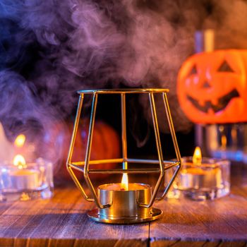 Halloween concept, orange pumpkin lantern and candles on a dark wooden table with blue-orange smoke around the background, trick or treat, close up