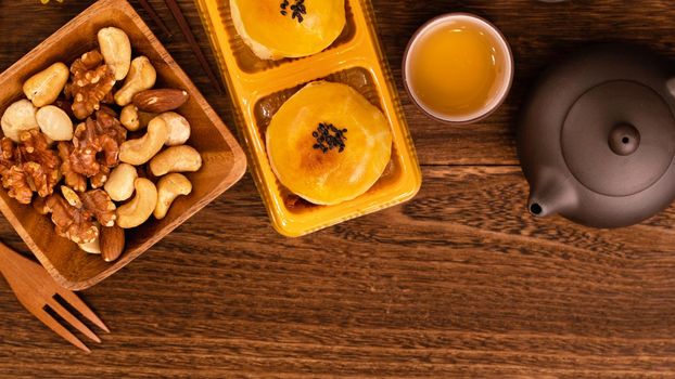 Moon cakes with tea on dark wooden table, holiday concept of Mid-Autumn festival traditional food layout design, top view, flat lay, copy space.