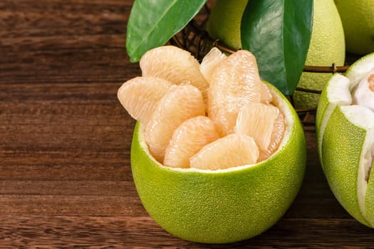 Fresh peeled pomelo, grapefruit, shaddock with green leaves on dark wooden plank table. Seasonal fruit near mid-autumn festival, close up, copy space