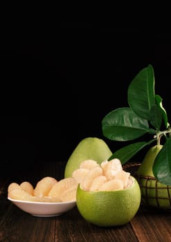 Fresh peeled pomelo, grapefruit, shaddock with green leaves on dark wooden plank table. Seasonal fruit near mid-autumn festival, close up, copy space