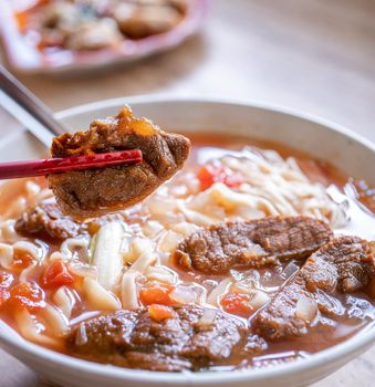 Beef noodle - Taiwan ramen meal with tomato sauce broth in bowl on bright wooden table, famous chinese style food, close up, top view, copy space
