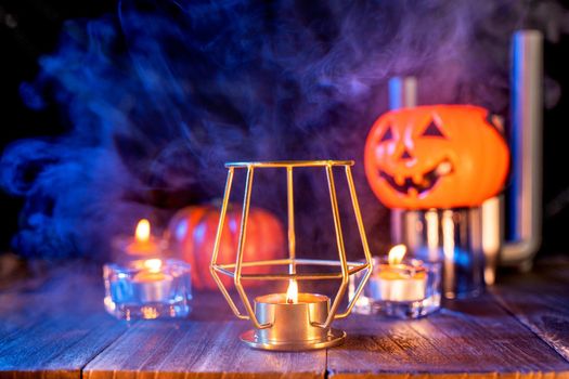 Halloween concept, orange pumpkin lantern and candles on a dark wooden table with green-orange smoke around the background, trick or treat, close up