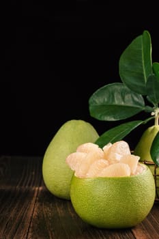 Fresh peeled pomelo, grapefruit, shaddock with green leaves on dark wooden plank table. Seasonal fruit near mid-autumn festival, close up, copy space
