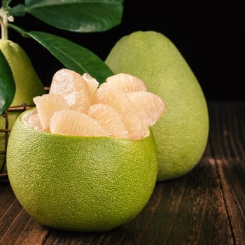 Fresh peeled pomelo, grapefruit, shaddock with green leaves on dark wooden plank table. Seasonal fruit near mid-autumn festival, close up, copy space