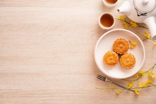 Moon cakes with tea on bright wooden table, holiday concept of Mid-Autumn festival traditional food layout design, top view, flat lay, copy space.