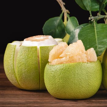 Fresh peeled pomelo, grapefruit, shaddock with green leaves on dark wooden plank table. Seasonal fruit near mid-autumn festival, close up, copy space