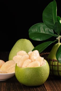 Fresh peeled pomelo, grapefruit, shaddock with green leaves on dark wooden plank table. Seasonal fruit near mid-autumn festival, close up, copy space