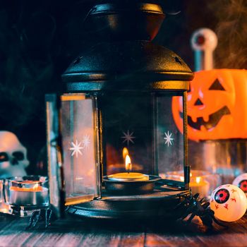 Halloween concept, spooky decorations with lighting up candle and candle holder with green tone smoke around on a dark wooden table, close up.