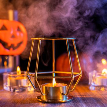 Halloween concept, spooky decorations with lighting up candle and candle holder with blue tone smoke around on a dark wooden table, close up.