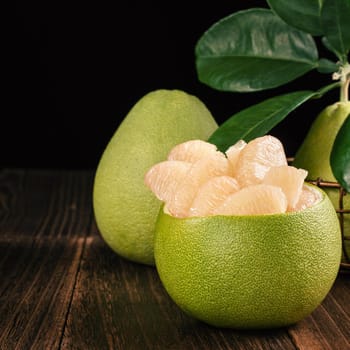 Fresh peeled pomelo, grapefruit, shaddock with green leaves on dark wooden plank table. Seasonal fruit near mid-autumn festival, close up, copy space