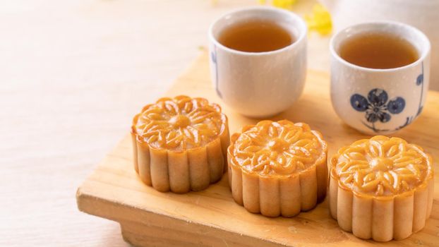 Moon cakes with tea on bright wooden table and serving try, holiday concept of Mid-Autumn festival traditional food layout design, close up, copy space.