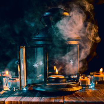 Halloween concept, spooky decorations with lighting up candle and candle holder with green tone smoke around on a dark wooden table, close up.