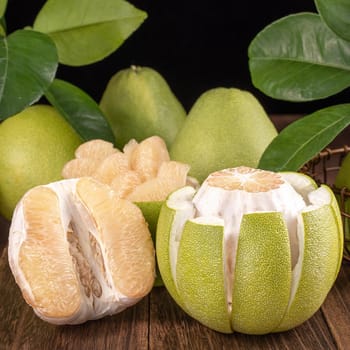 Fresh peeled pomelo, grapefruit, shaddock with green leaves on dark wooden plank table. Seasonal fruit near mid-autumn festival, close up, copy space